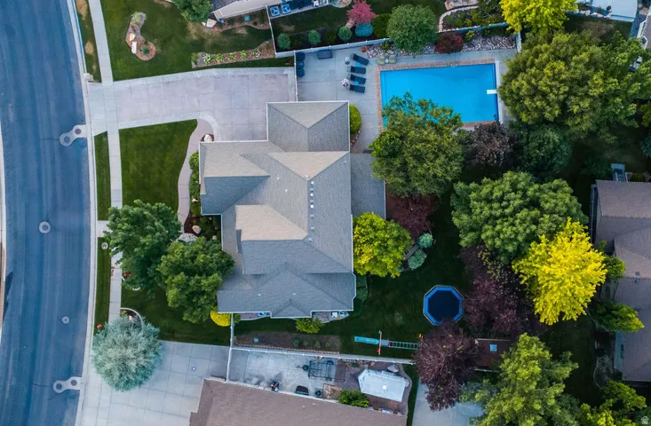 Expansive property featuring a multi-gabled residence, a large rectangular swimming pool with a diving board, a concrete patio area, mature landscaping, and a manicured lawn