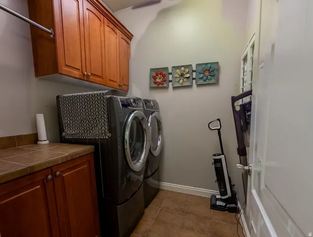 Dedicated laundry area featuring a built-in wood-finish cabinetry, tile flooring, a tile countertop, and an overhead hanging rod