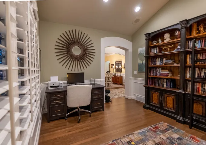 Dedicated office space featuring built-in bookcases, wood-finish flooring, and natural light from plantation-shutter windows