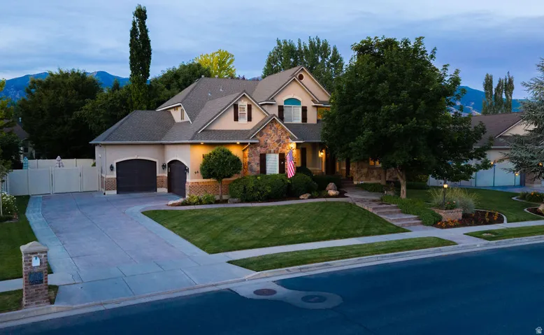Stucco and stone facade property with a multi-car driveway, a meticulously landscaped front yard, and mature trees