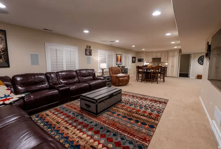 Spacious lower-level living area with recessed lighting, built-in wall speakers, and plantation shutters