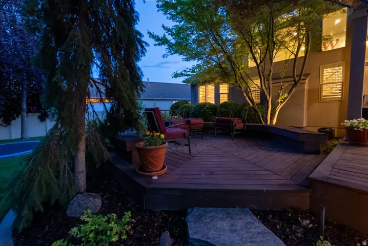 Expansive multi-level wood-finish deck featuring built-in bench seating, mature landscaping, and accent lighting