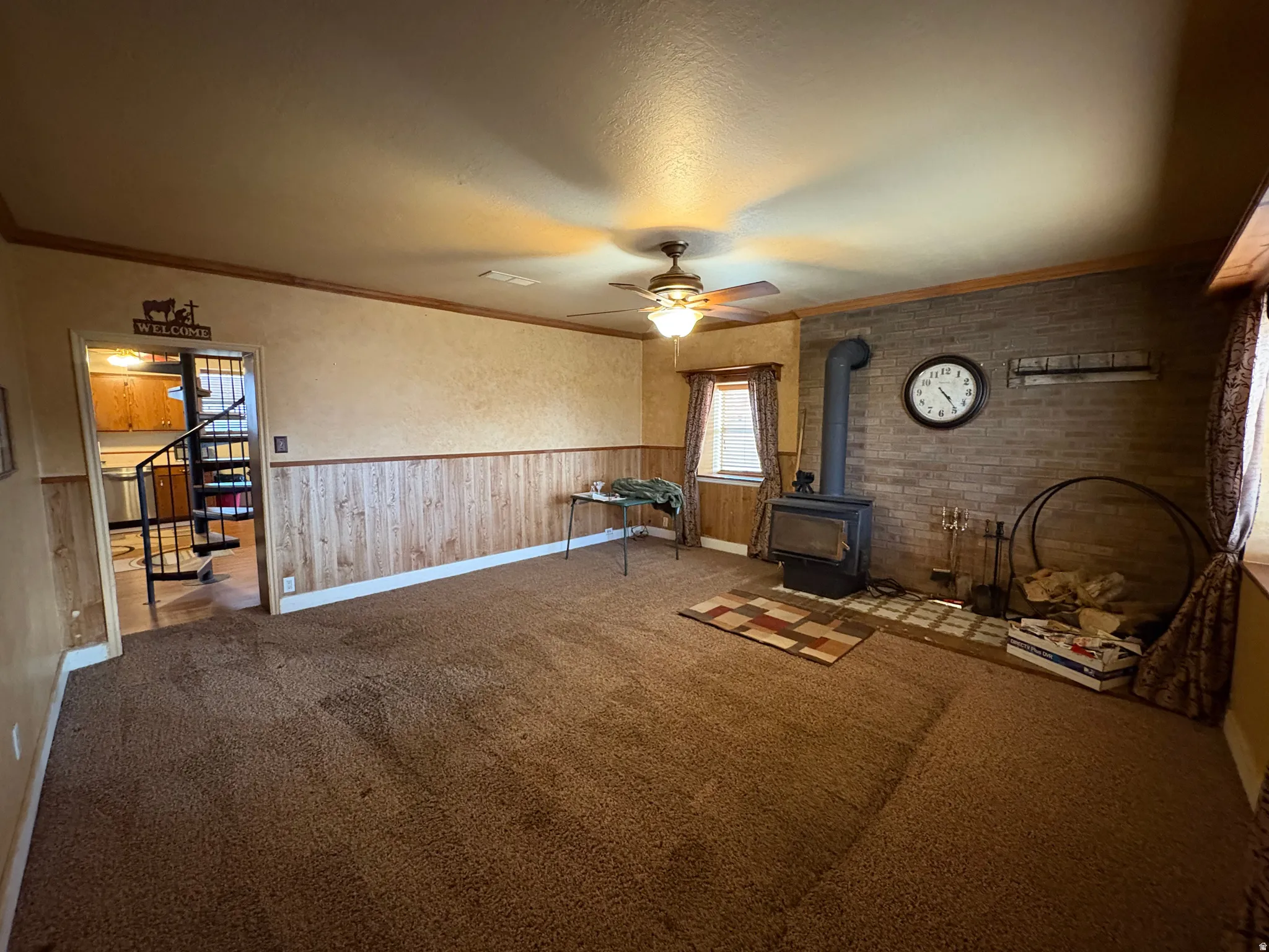 Spacious living area featuring a brick accent wall with a wood-burning stove, wall-to-wall carpeting, and wood-paneled wainscoting