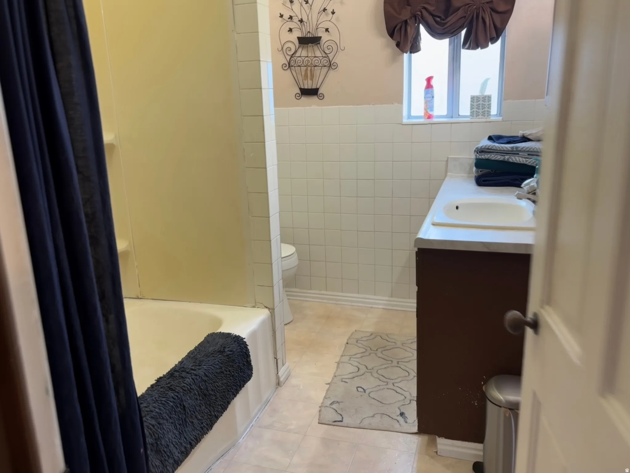 Bathroom featuring a single vanity with a white countertop and integrated sink, a built-in tub with a shower surround, and white tile wainscoting