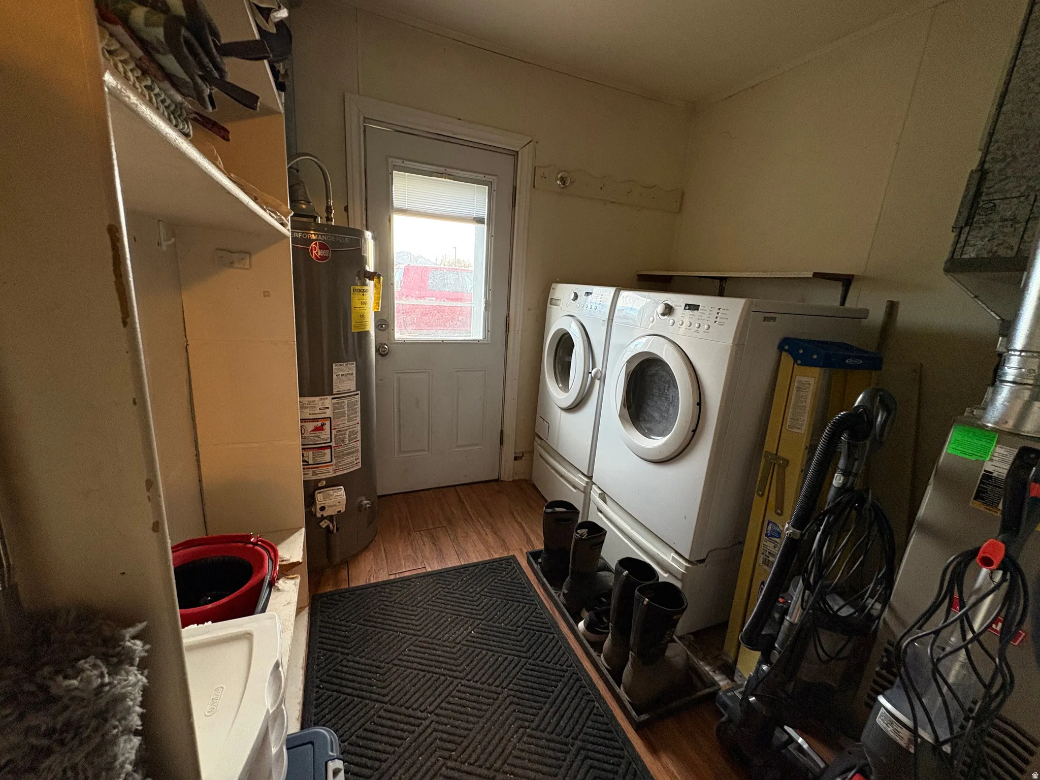 Utility room featuring wood-finish flooring, built-in shelving, water heater, and a rear door with an upper window