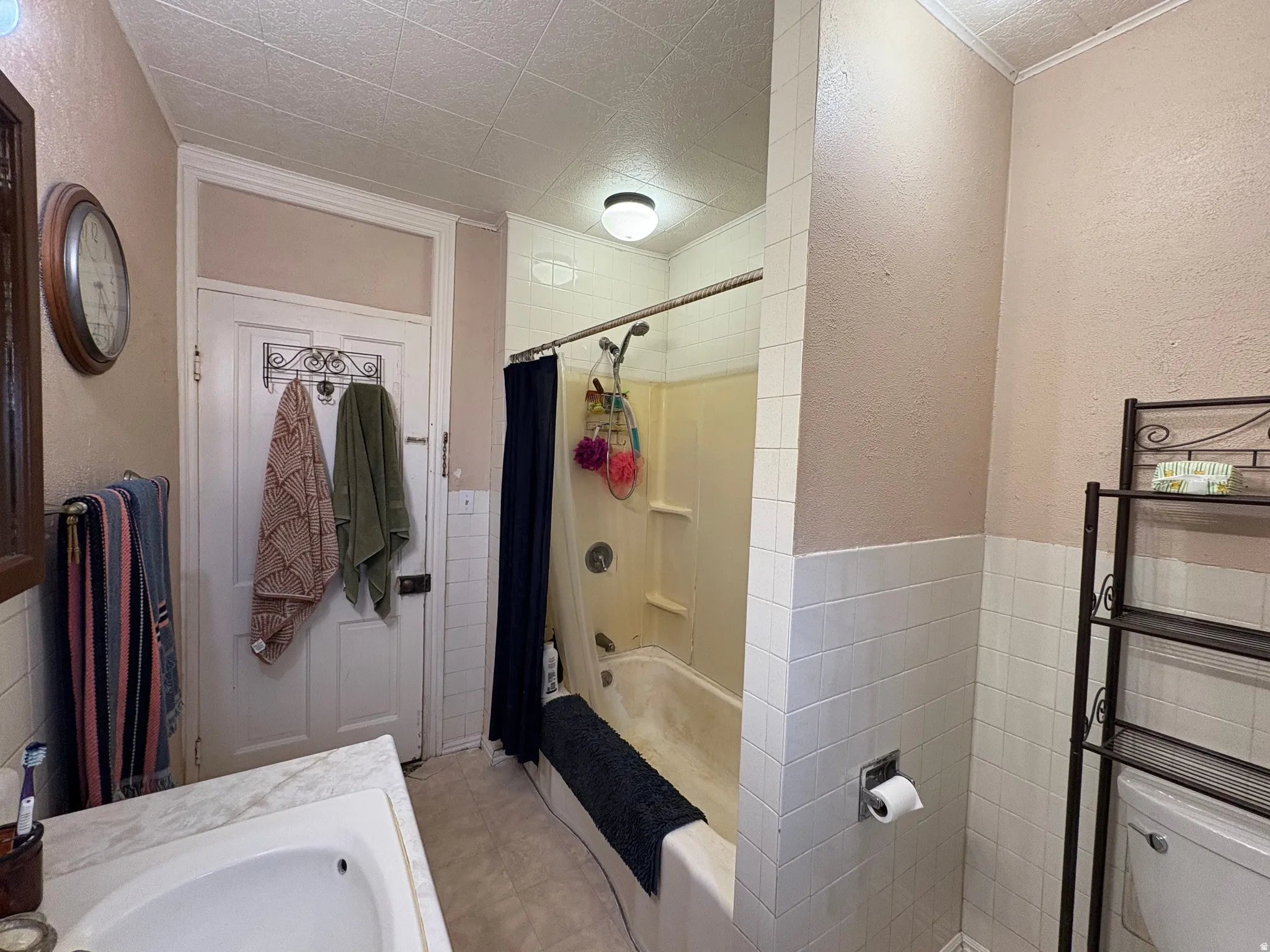 Bathroom featuring a built-in tub with shower, white tile wainscoting, a vanity with an integrated sink, a traditional door, and a textured ceiling