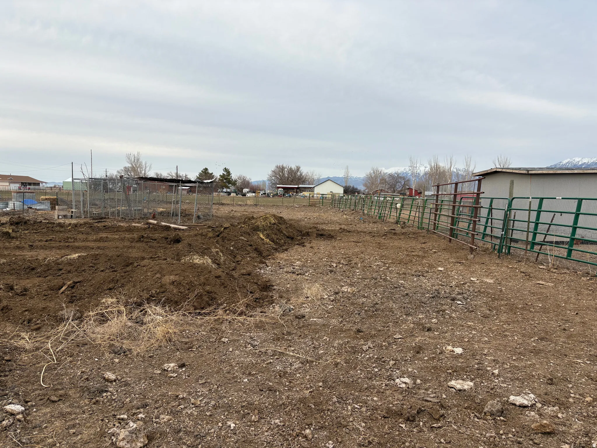 Expansive open lot featuring a large area of tilled earth, multiple sections of metal fencing, and a compact shed