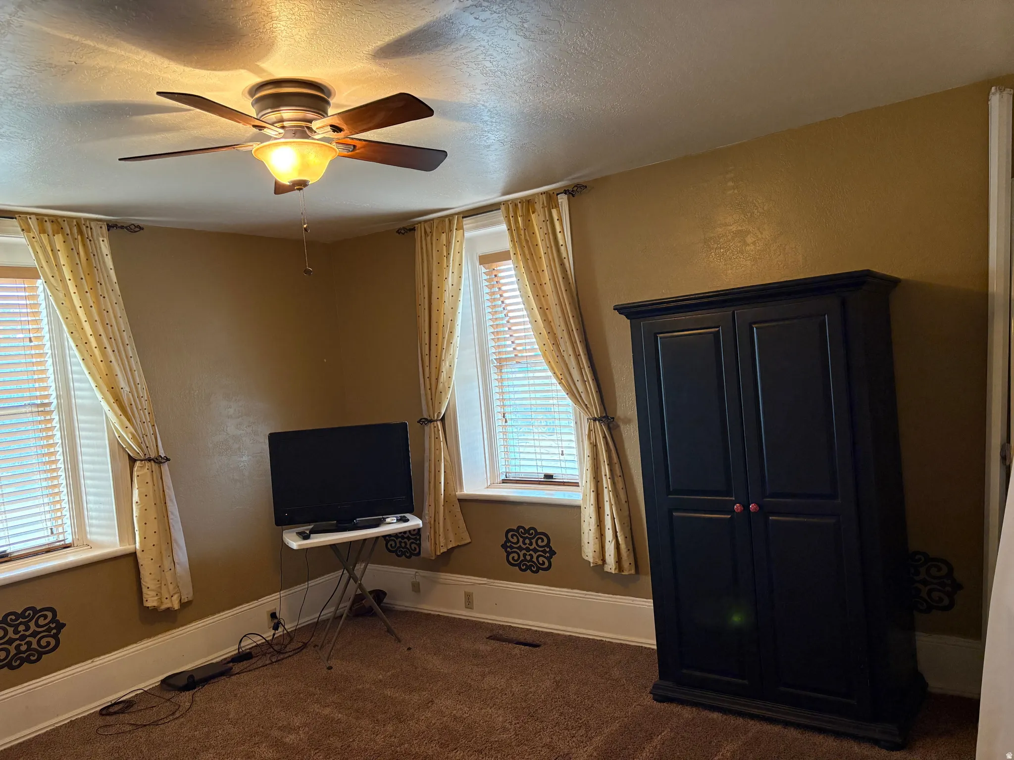 Carpeted room featuring a ceiling fan with light fixture, window blinds, and decorative wall accents