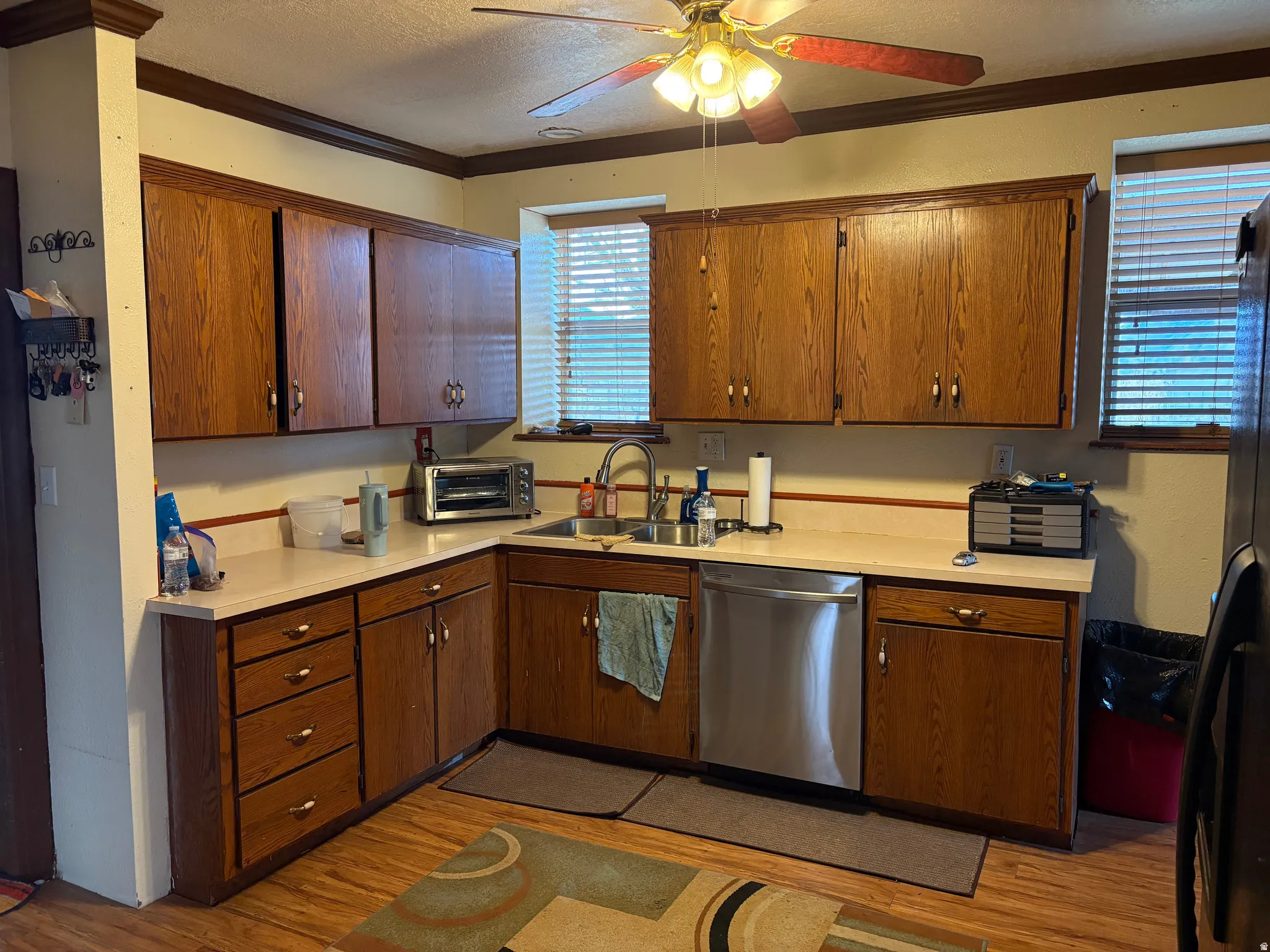 Kitchen featuring wood-finish cabinetry, light-toned countertops, and a stainless steel dishwasher