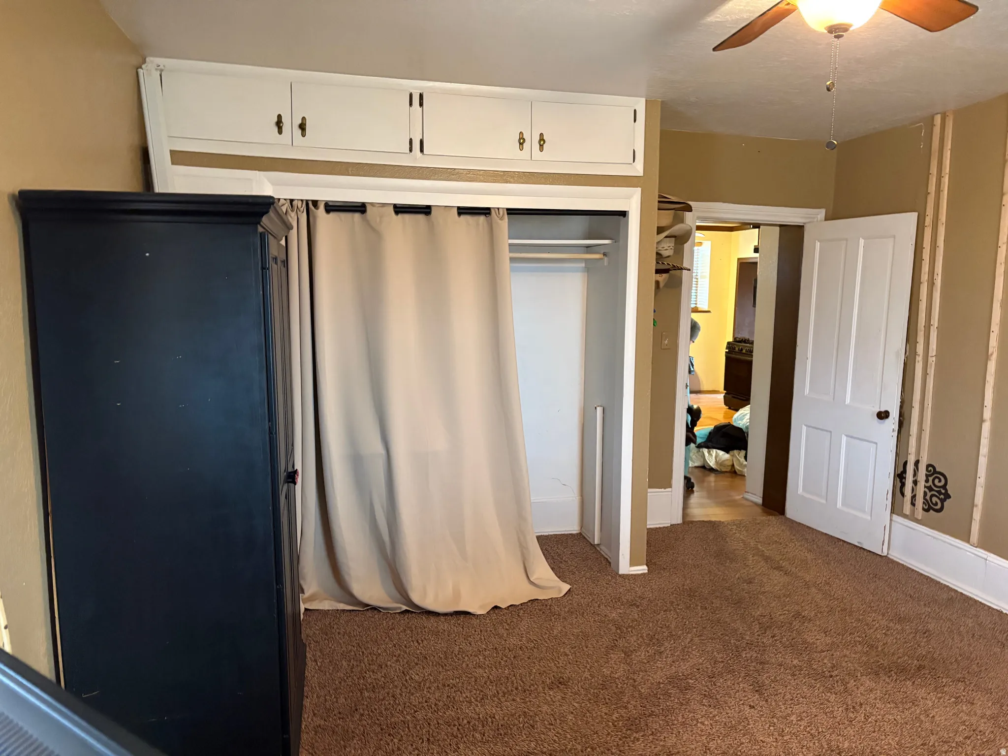 Room featuring built-in overhead cabinetry, a ceiling fan with light fixture, and a closet with a curtain enclosure