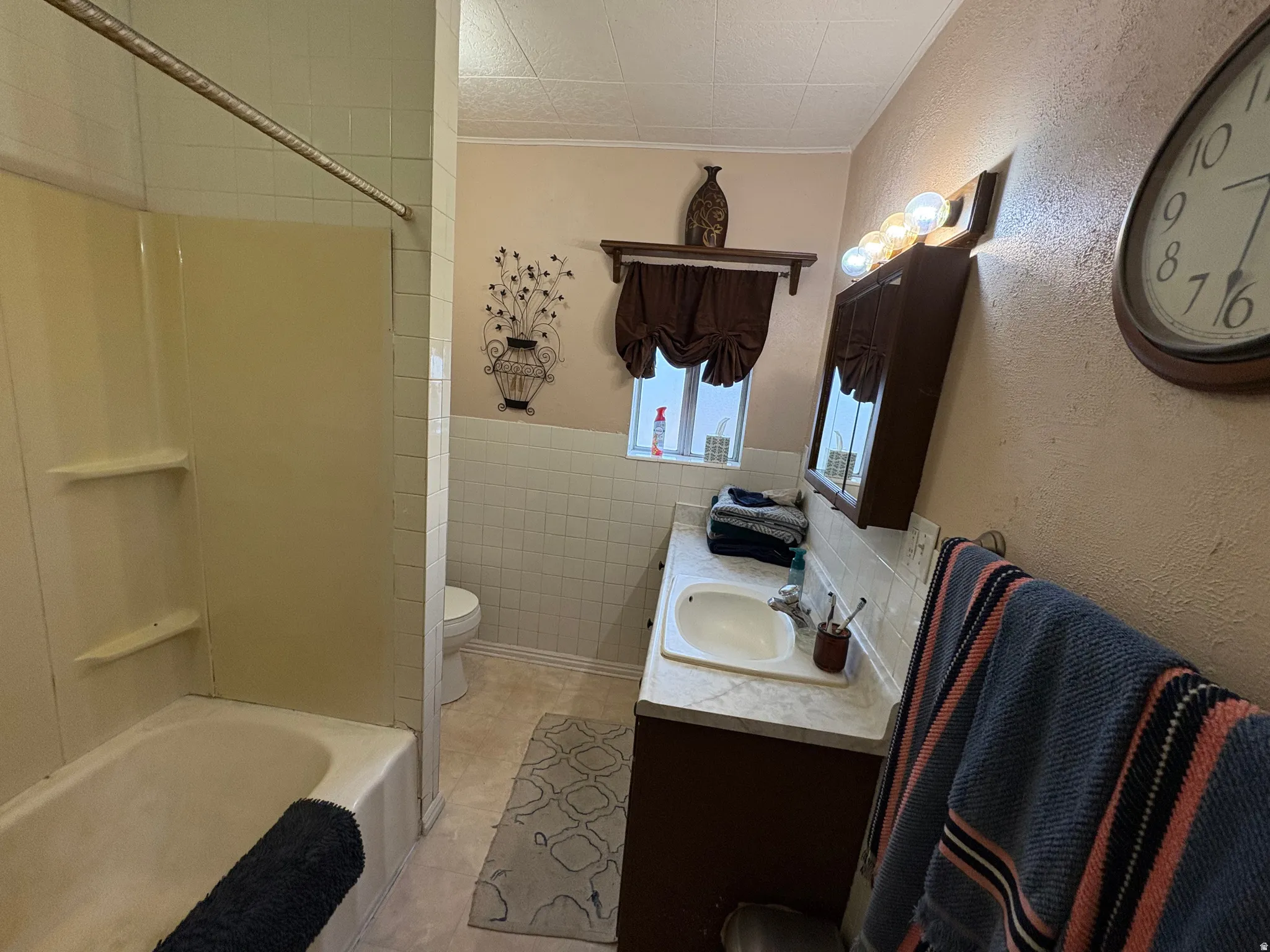 Bathroom featuring a shower-tub combination with integrated shelving, tile wall surround, and a single vanity with an integrated sink and base cabinet