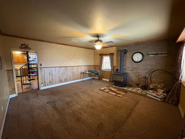 Spacious living area featuring a brick accent wall with a wood-burning stove, wall-to-wall carpeting, and wood-paneled wainscoting