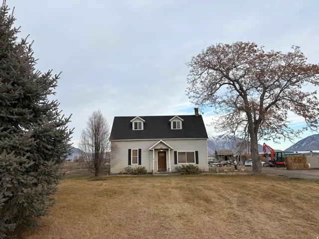 Dormered colonial-style home featuring light-colored siding, dark shutters, and a dark shingle roof