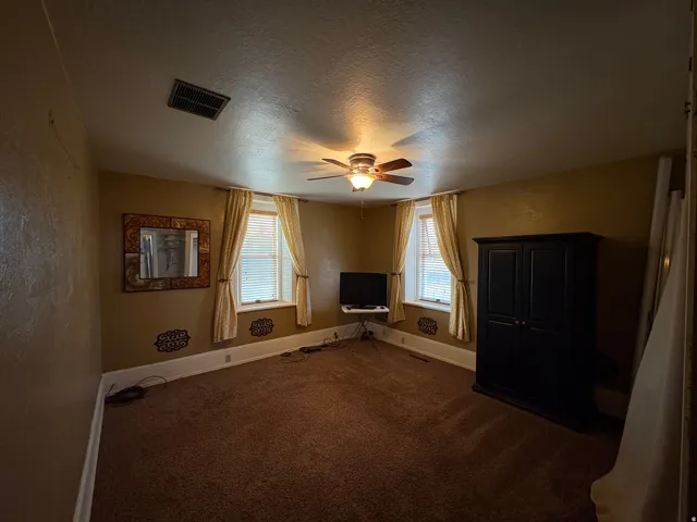 Carpeted interior space featuring a ceiling fan with integrated lighting, two windows with blinds, and white trim molding