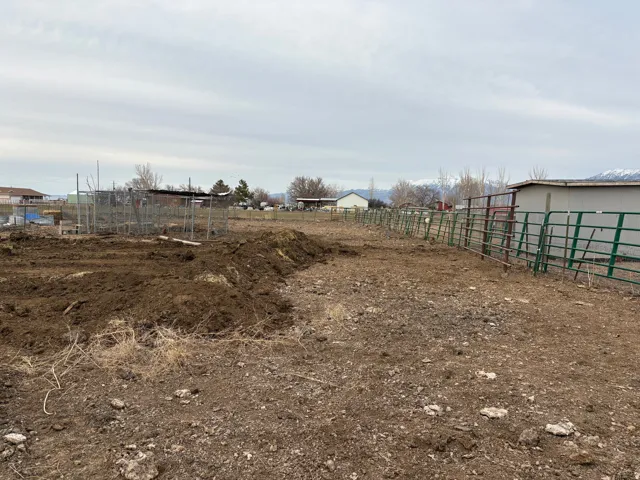 Expansive open lot featuring a large area of tilled earth, multiple sections of metal fencing, and a compact shed