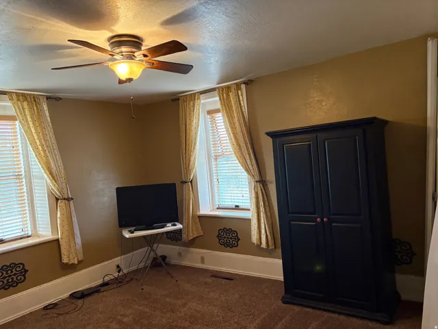 Carpeted room featuring a ceiling fan with light fixture, window blinds, and decorative wall accents