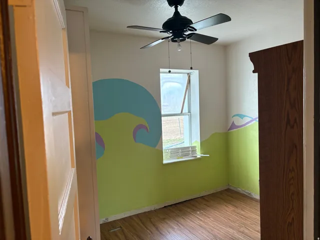 Room featuring wood-finish flooring, a ceiling fan, and a window with a sill