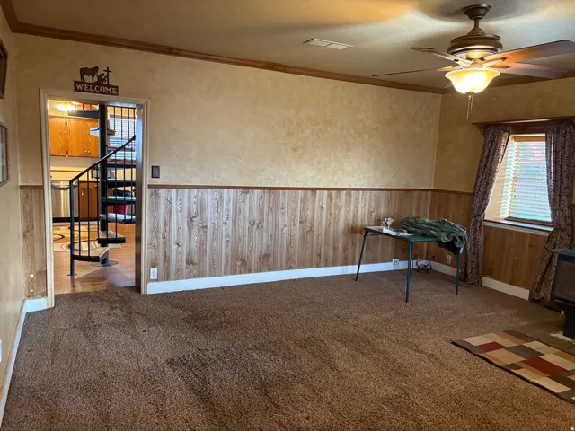 Spacious room featuring carpeting, wood-finish wainscoting, and a ceiling fan with integrated lighting