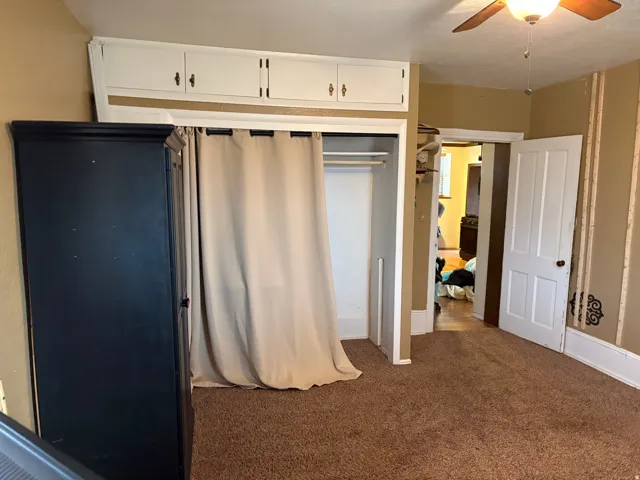 Room featuring built-in overhead cabinetry, a ceiling fan with light fixture, and a closet with a curtain enclosure