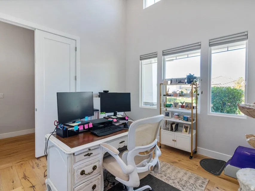 Office space featuring high ceilings, multiple large windows, wood-finish flooring, and a white pocket door