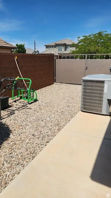 Gravel side yard featuring a block wall, metal gate, concrete walkway, and an external air conditioning unit