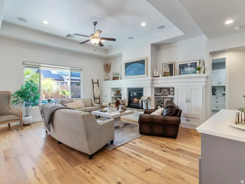 Living area featuring wood-finish flooring, a contemporary fireplace with mantel, built-in shelving, recessed lighting, and a ceiling fan