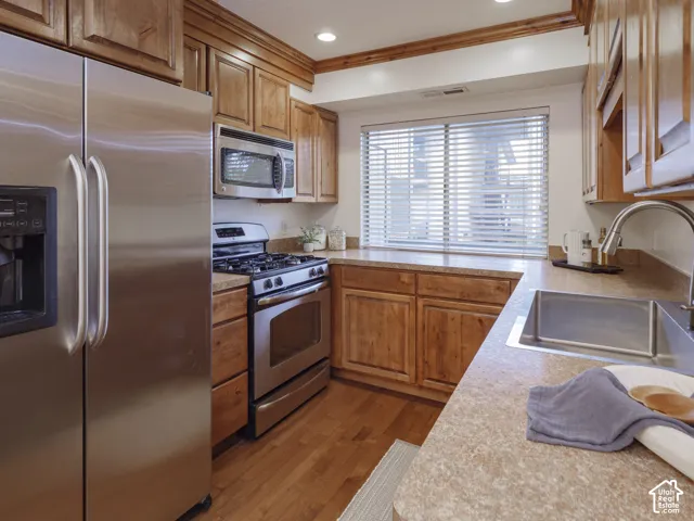 Kitchen featuring wood cabinetry, stainless steel appliances, solid-surface countertops, an undermount stainless steel sink with a goose-neck faucet, and wood-finish flooring