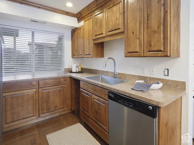 Kitchen featuring wood cabinetry, integrated stone-composite countertops, stainless steel undermount sink with gooseneck faucet, stainless steel dishwasher, and wood-finish flooring
