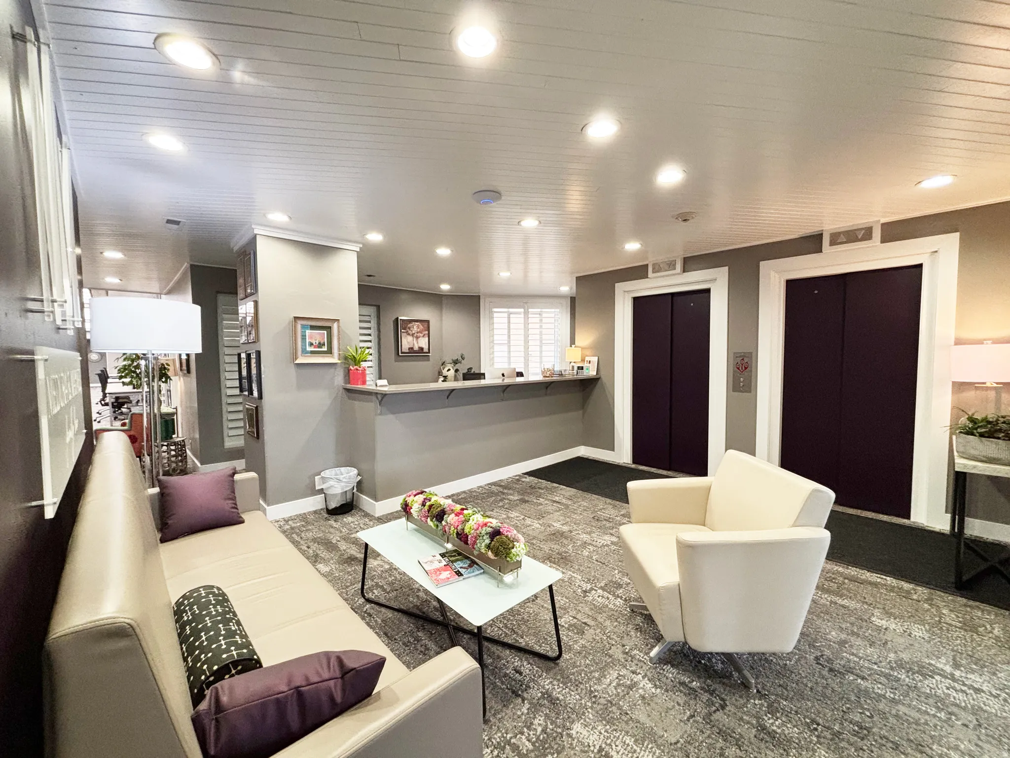 Lobby reception area featuring two elevator entrances with dark doors and light trim, a reception counter, and recessed lighting
