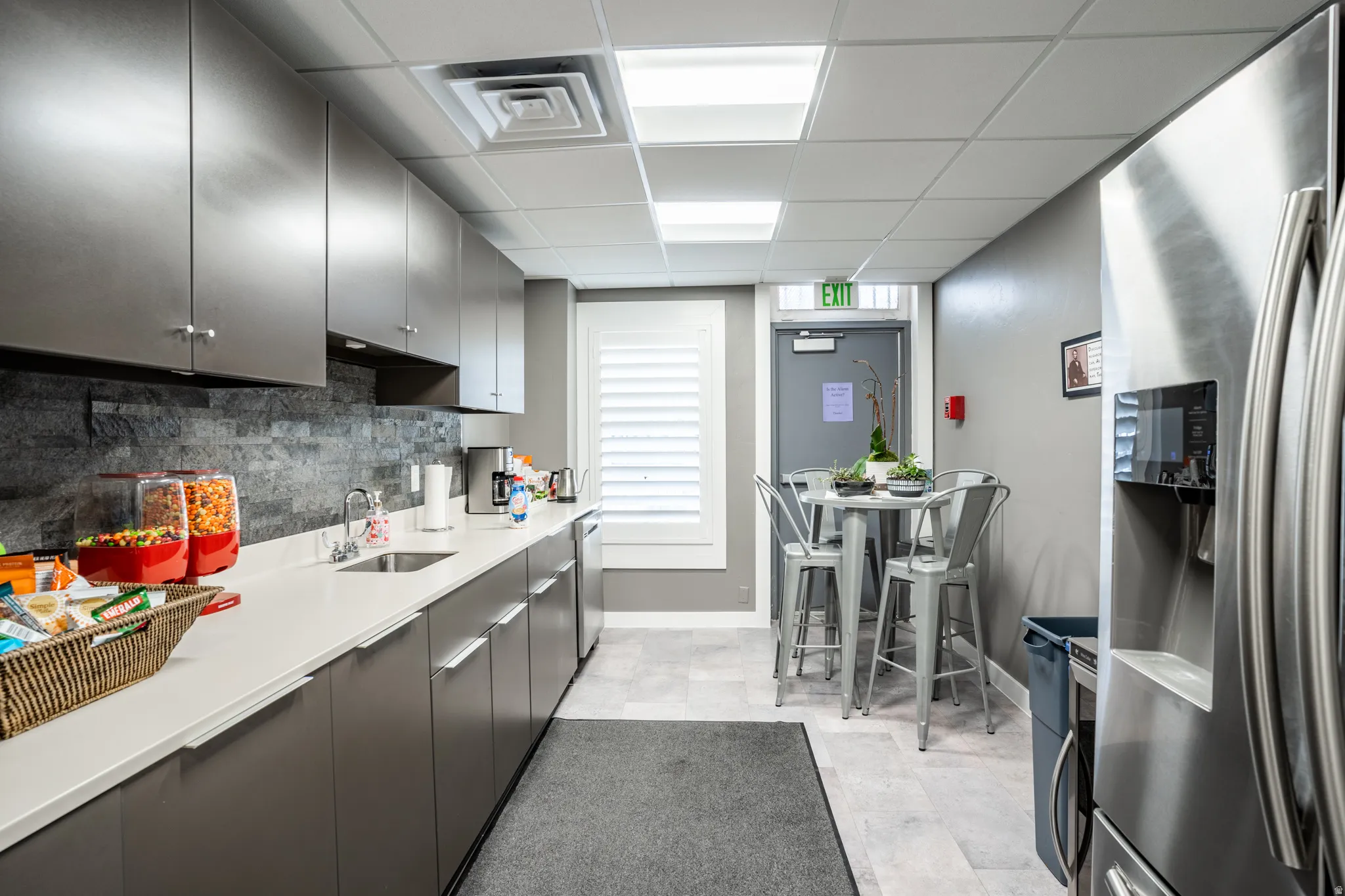 Modern kitchen space featuring extensive upper and lower cabinetry, a stainless steel refrigerator, white countertops, a stone-finish backsplash, and light-toned flooring
