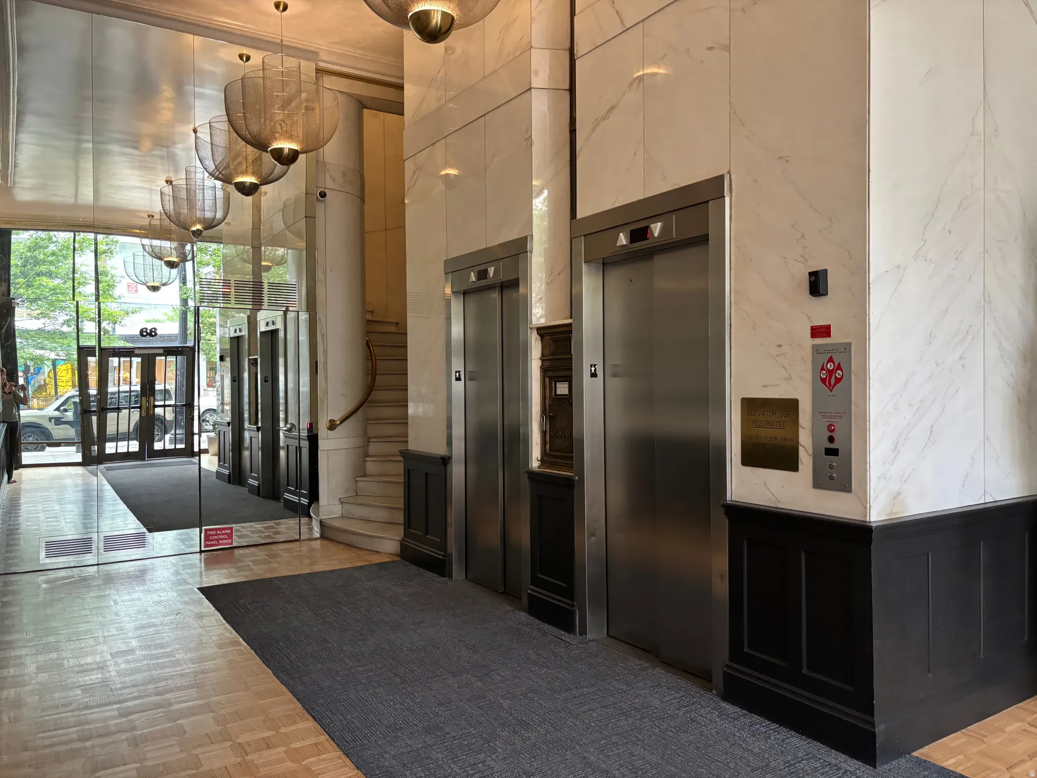 Lobby featuring two elevators with stainless steel doors, white marble-finish wall panels, and dark wood wainscoting