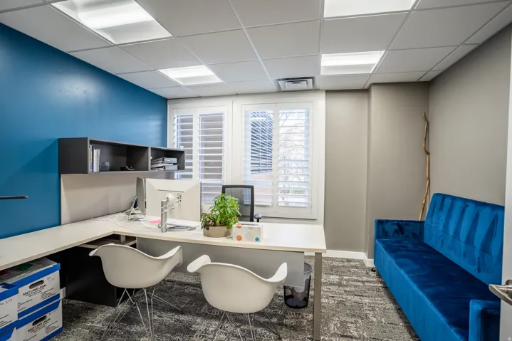 Office space featuring a vibrant accent wall, drop ceiling with recessed lighting, integrated shelving, and plantation shutters
