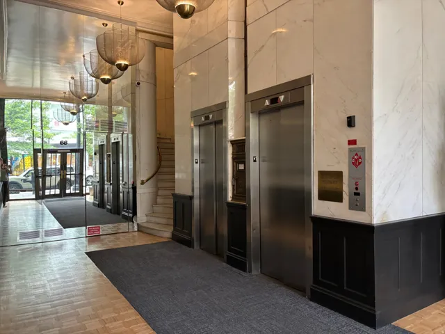 Lobby featuring two elevators with stainless steel doors, white marble-finish wall panels, and dark wood wainscoting