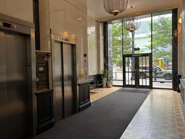 Lobby entry featuring two stainless steel elevators, patterned marble walls, and wood-finish flooring