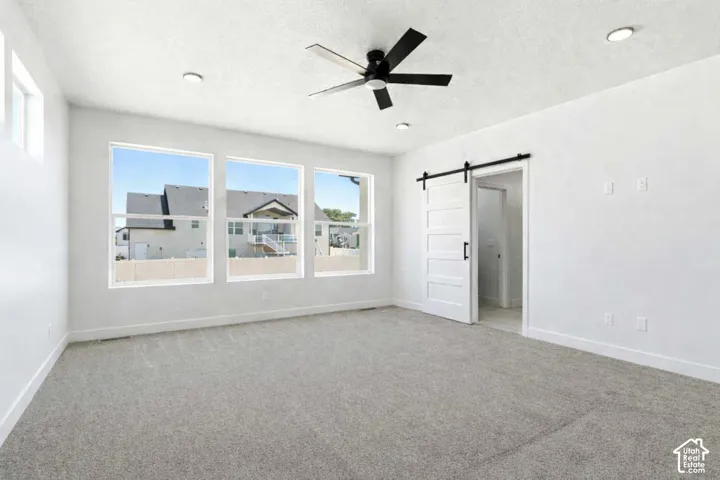 Spacious room featuring three large windows, light gray carpet, and a modern black ceiling fan