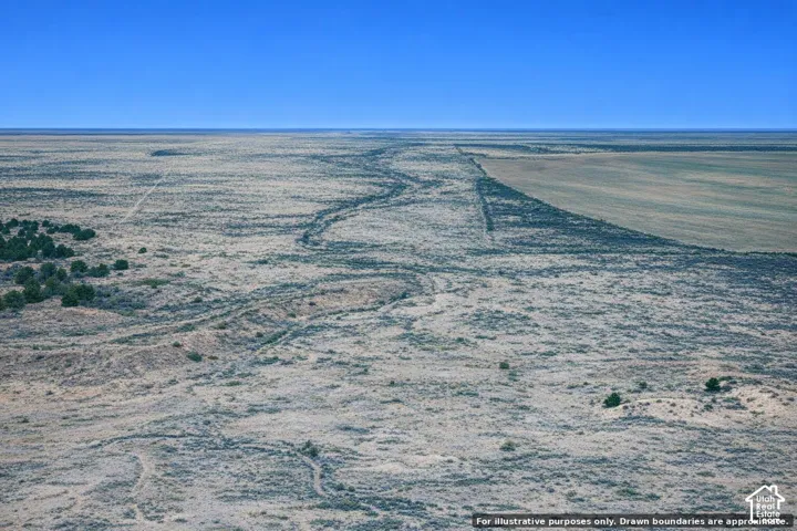 Expansive land parcel featuring natural desert vegetation, clear blue sky, and distant cultivated fields