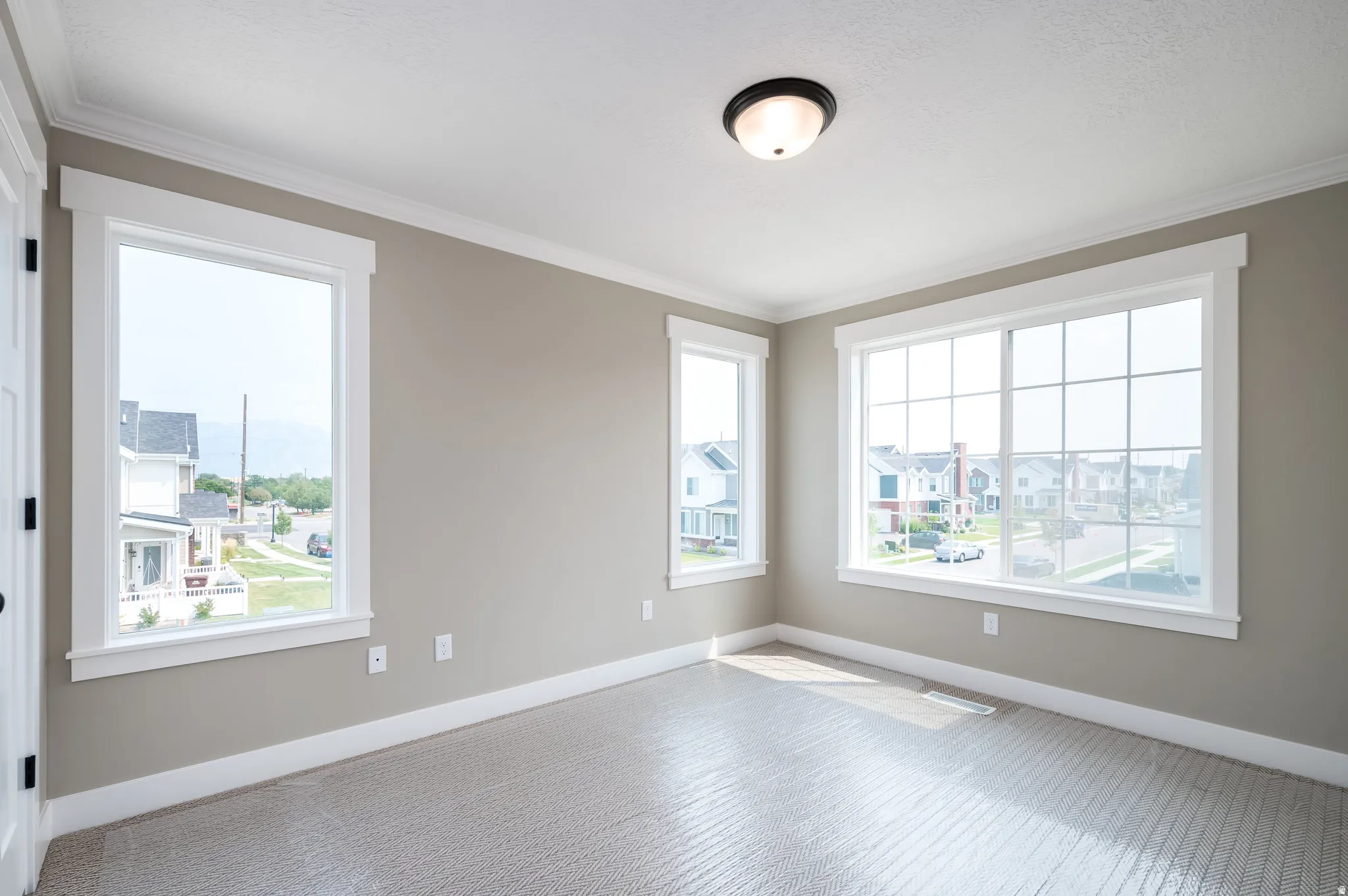 Room featuring three windows with white trim, light gray walls, and textured carpet flooring