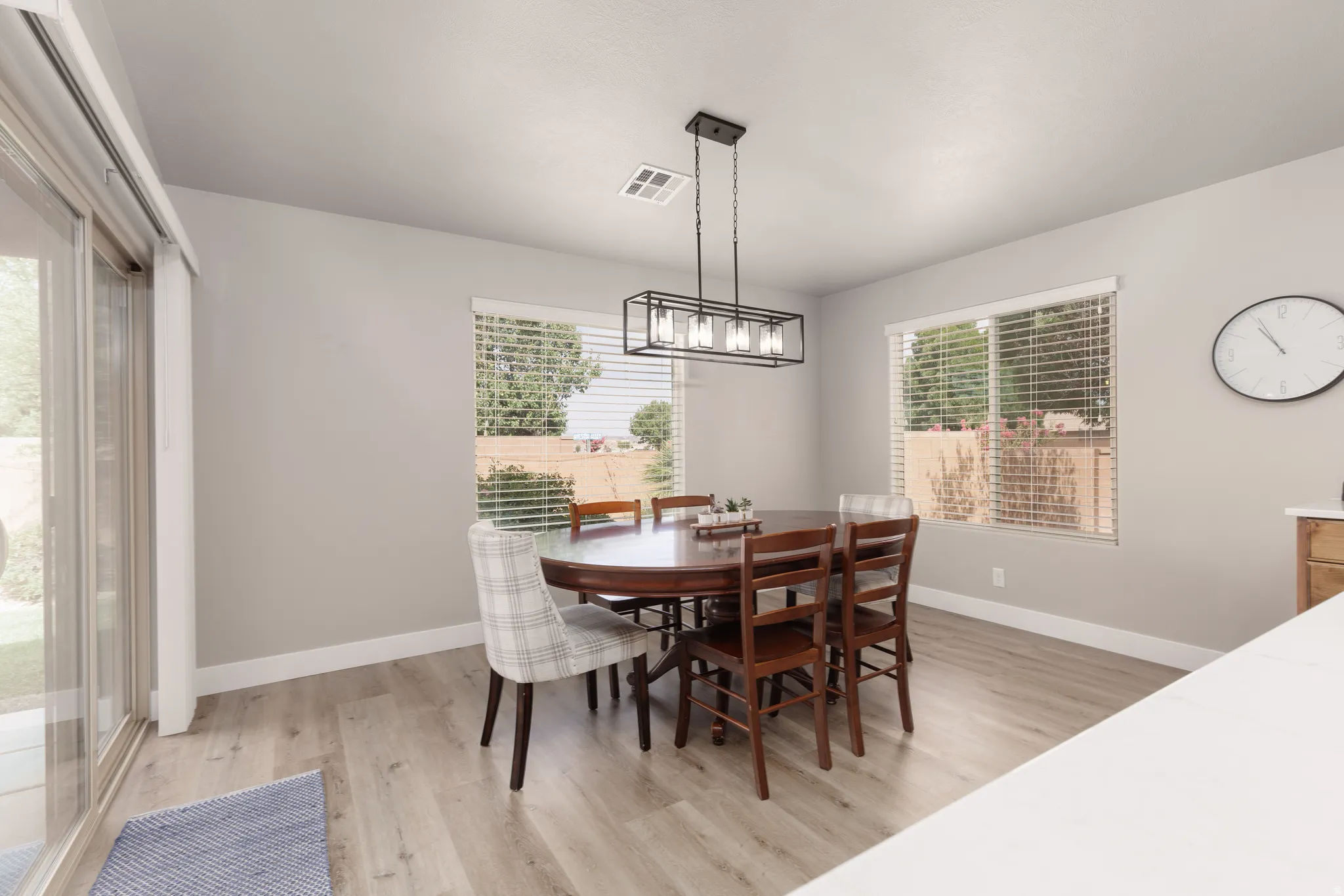 Spacious dining area featuring LVP flooring, two large windows with horizontal blinds, and a contemporary linear chandelier