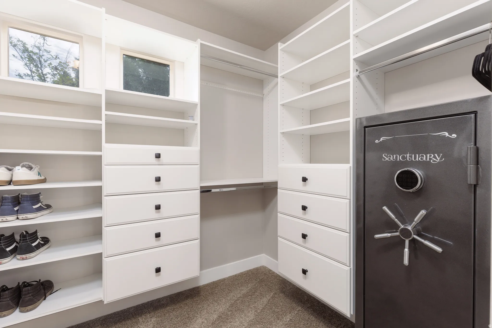 Custom closet system featuring extensive shelving, multiple hanging sections, built-in drawers with dark hardware, and natural light from transom windows