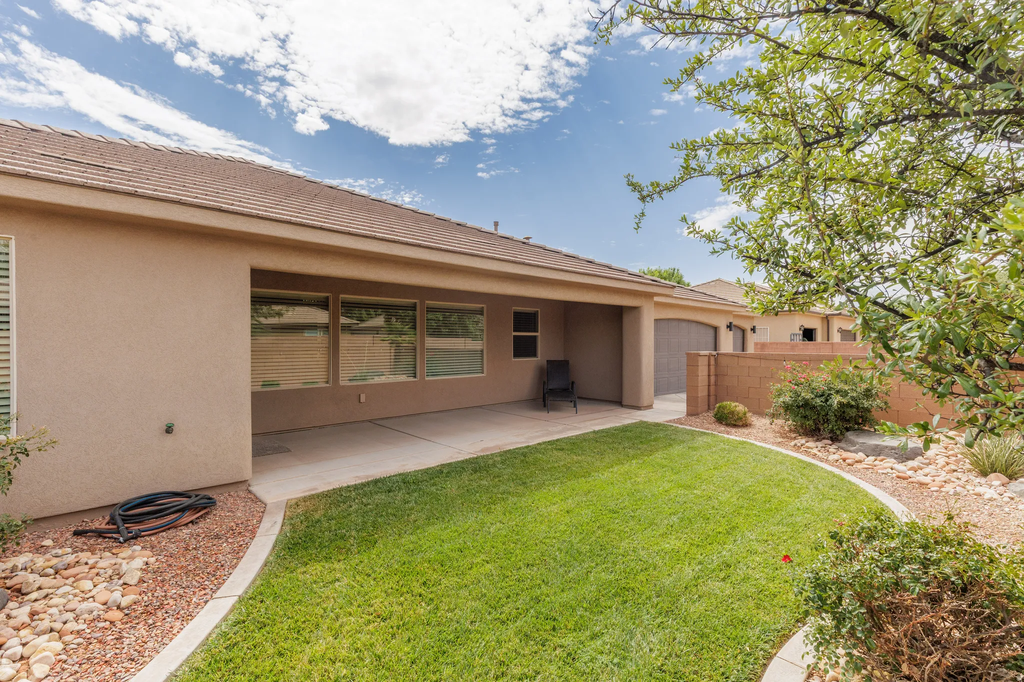 Expansive backyard featuring a manicured lawn, established landscaping, large covered patio and a privacy wall