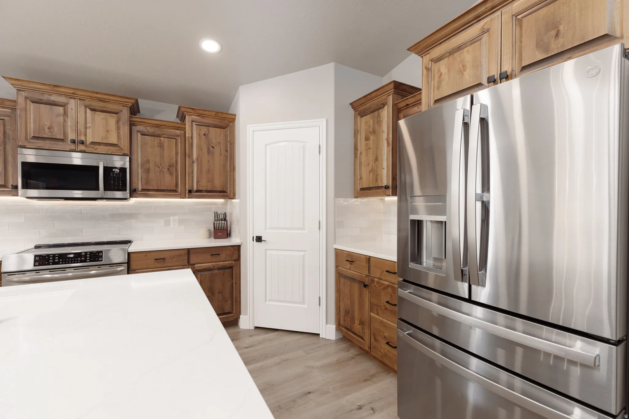 Kitchen featuring wood cabinetry, stainless steel appliances, white subway tile backsplash, white countertops, and LVP flooring