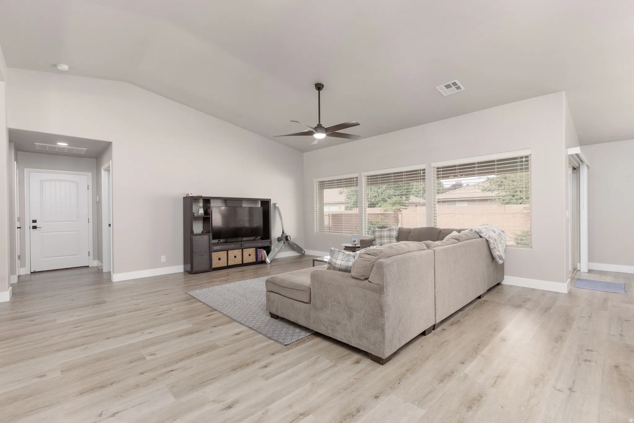 Spacious living area featuring vaulted ceilings, a ceiling fan with integrated lighting, and multiple windows with horizontal blinds