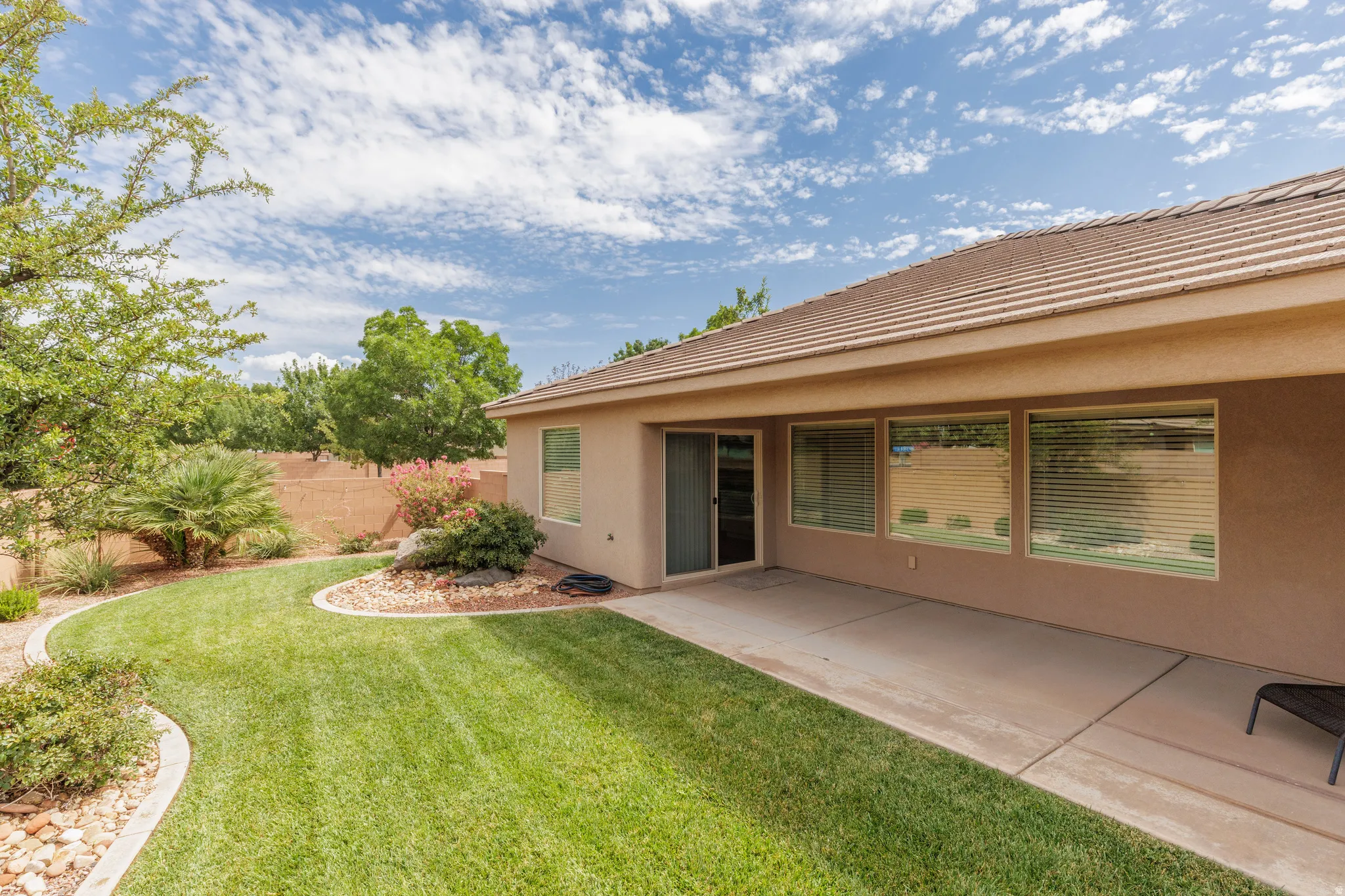 Expansive backyard featuring a manicured lawn, established landscaping, large covered patio and a privacy wall