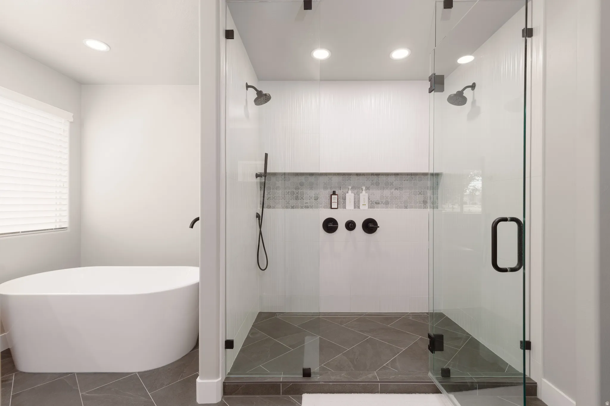 Primary ensuite bathroom with custom walk-in glass enclosure shower with dual shower heads large niche and soaking tub