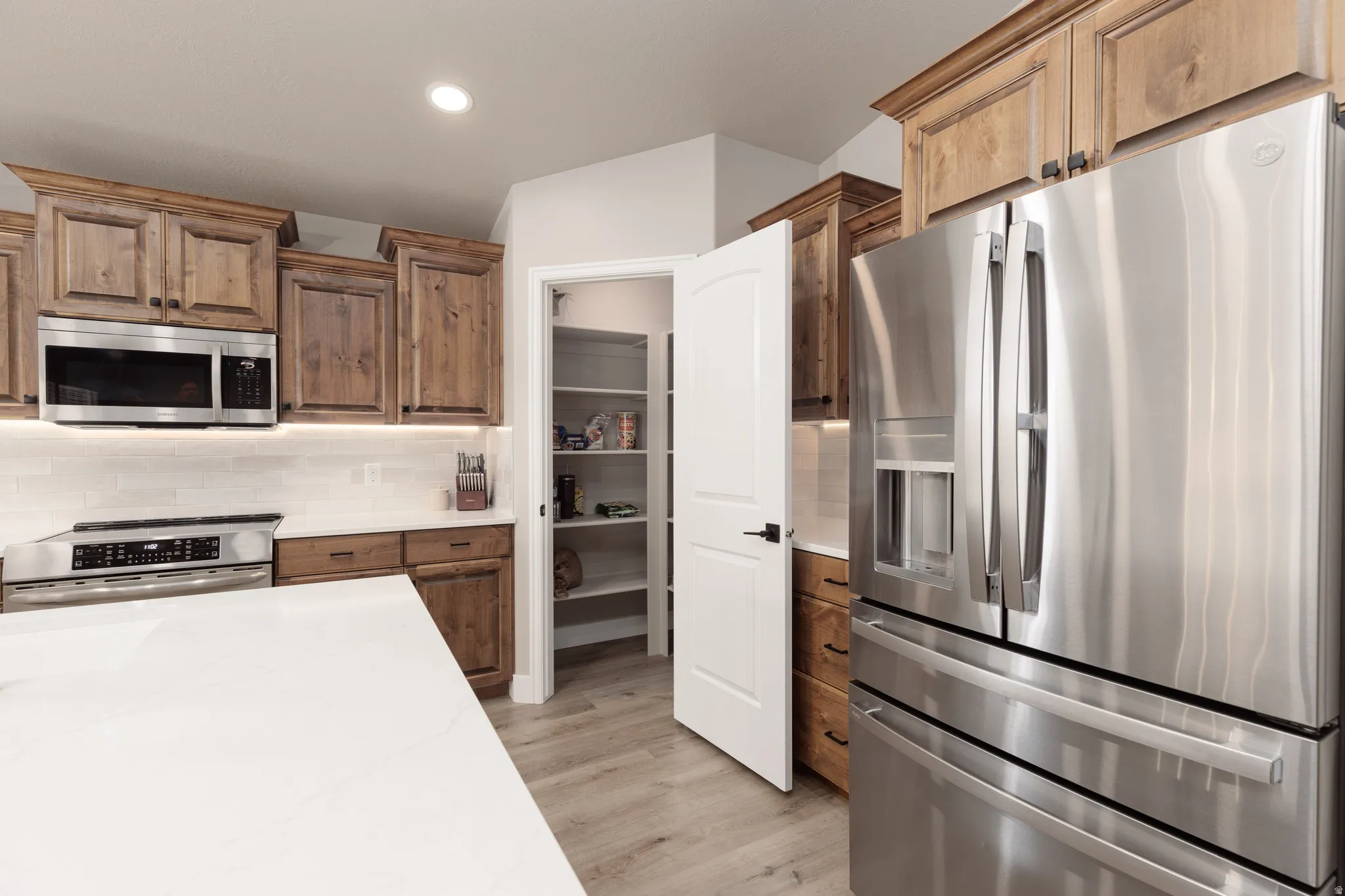 Kitchen featuring wood cabinetry, stainless steel appliances, white subway tile backsplash, white countertops, and LVP flooring
