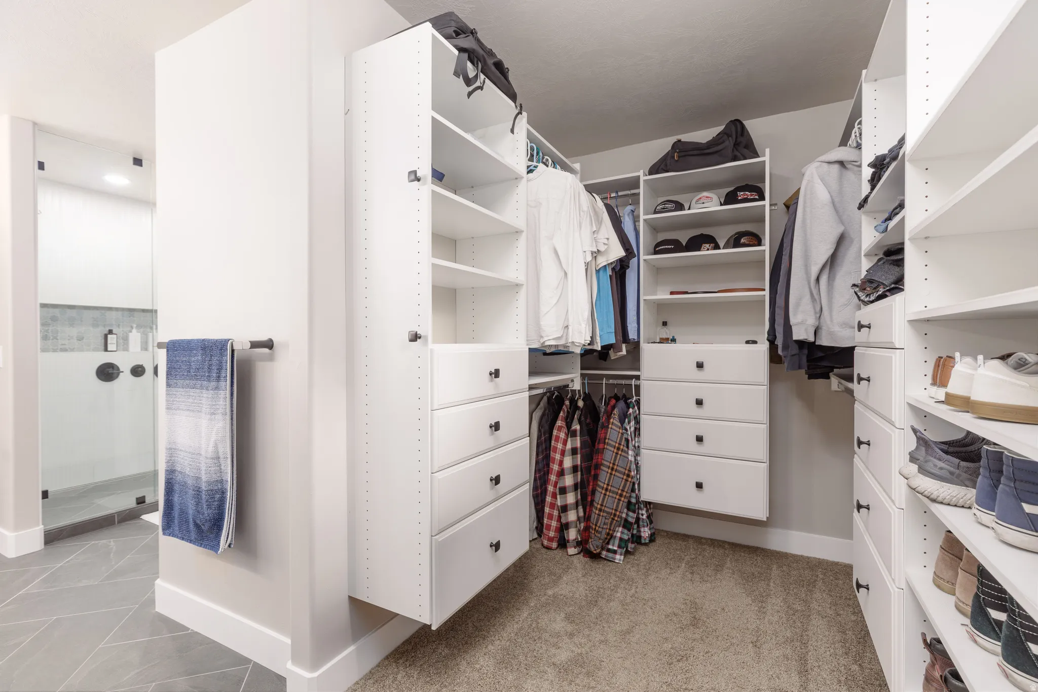 Custom closet organization system featuring white cabinetry with black hardware, extensive shelving, integrated drawer storage, and multiple hanging rods