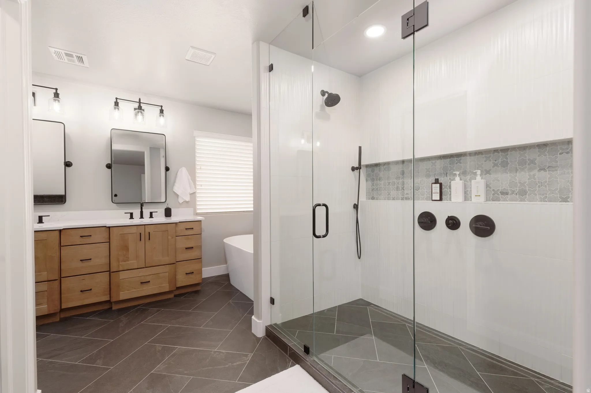 Primary ensuite featuring custom dual shower heads, dark-toned fixtures and a decorative tiled niche