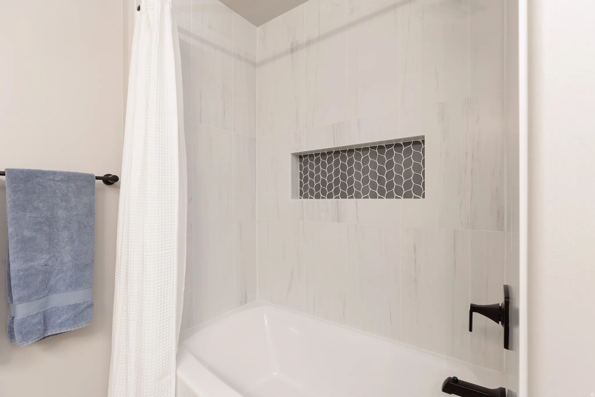 Bathtub with white subway tile surround, recessed niche with geometric mosaic tile, and matte black fixtures