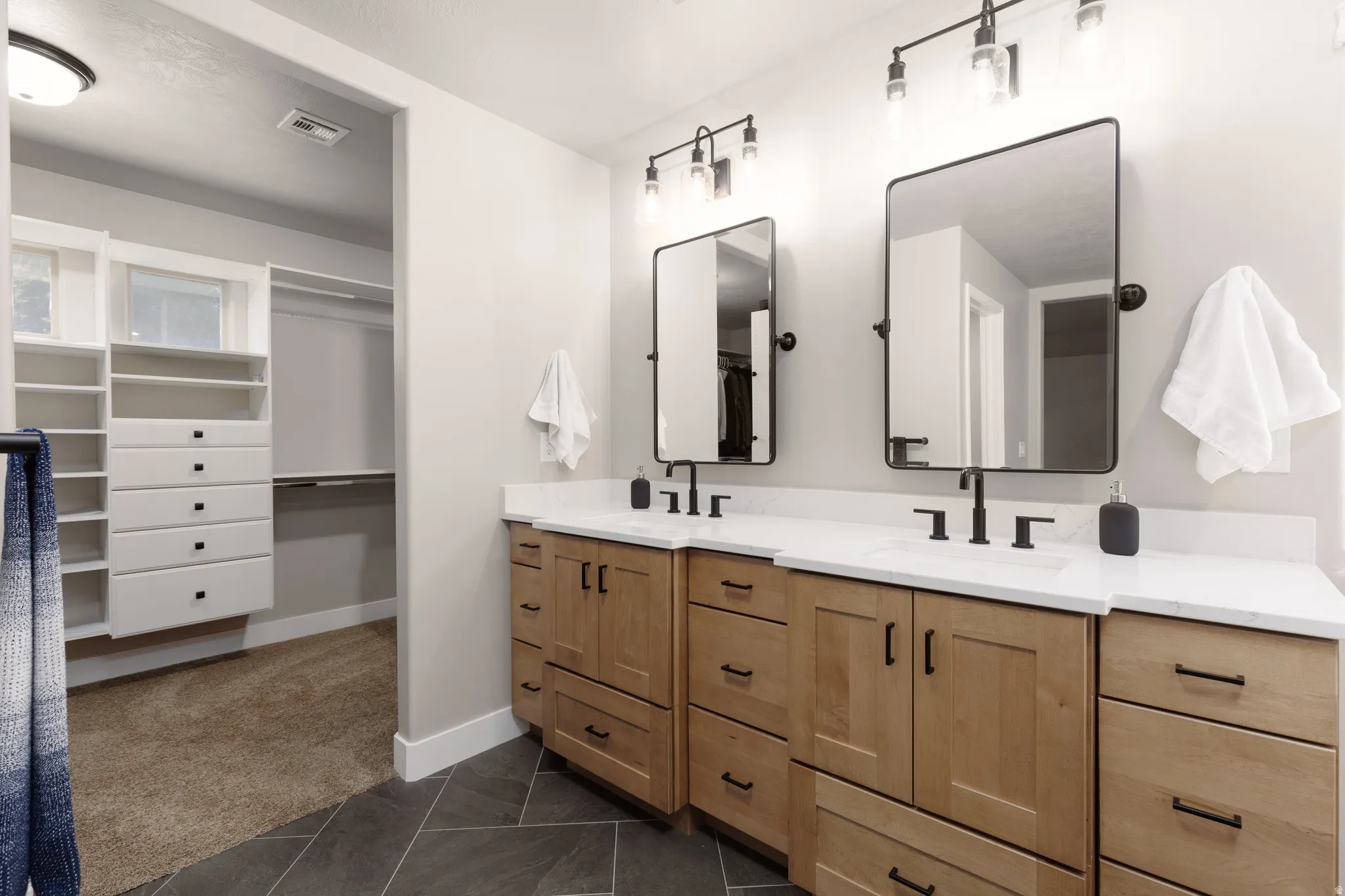 Dual light wood-finish vanities with white countertops and matte black hardware