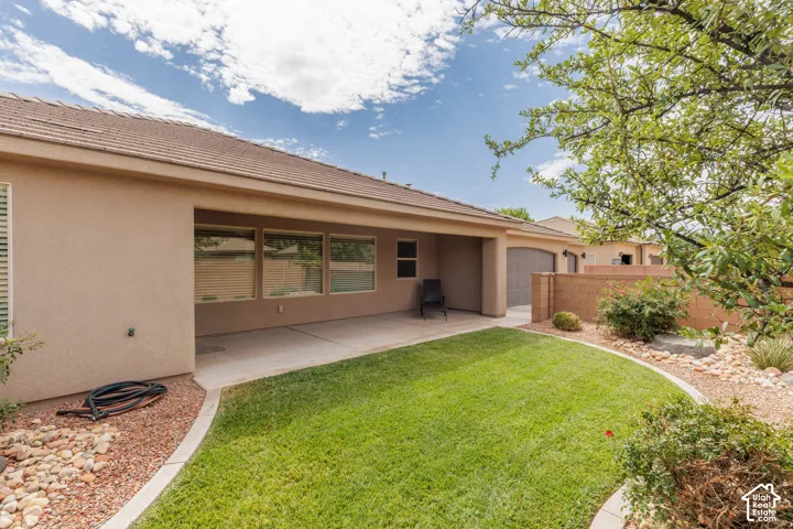 Expansive backyard featuring a manicured lawn, established landscaping, large covered patio and a privacy wall